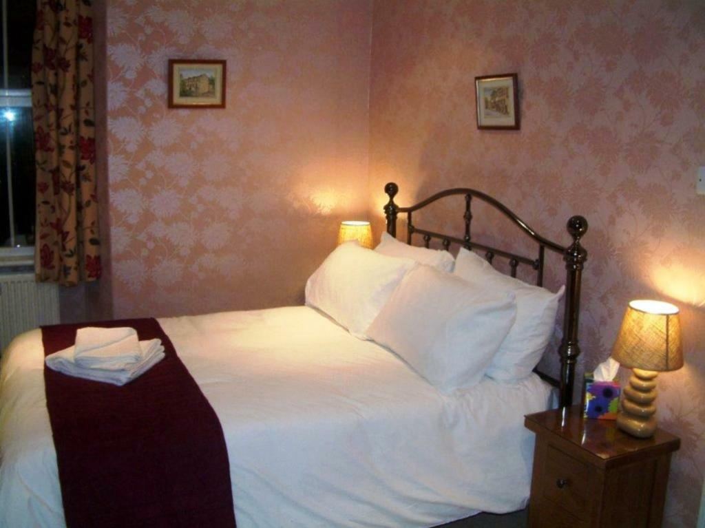 Double guest room with brass bed, pink floral wallpaper and burgundy bed runner